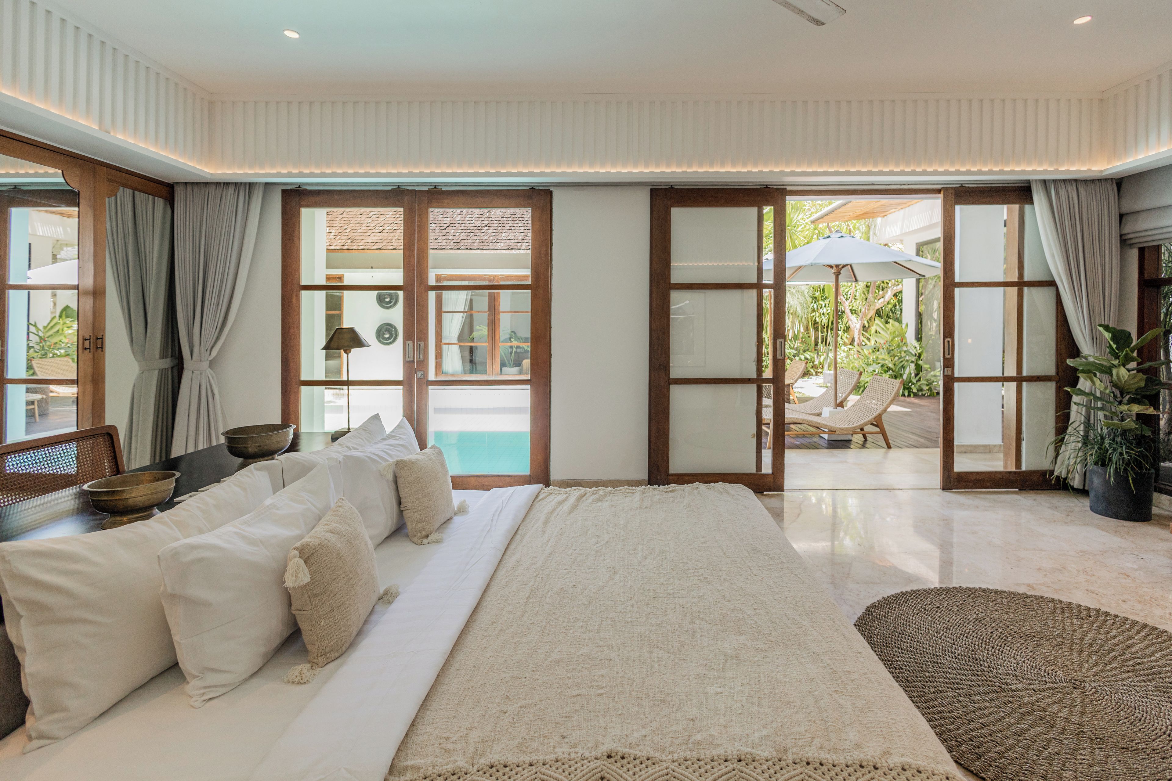 A spacious bedroom with a large bed, a sitting area with a table and chairs, and a view of the outdoor area through glass doors.