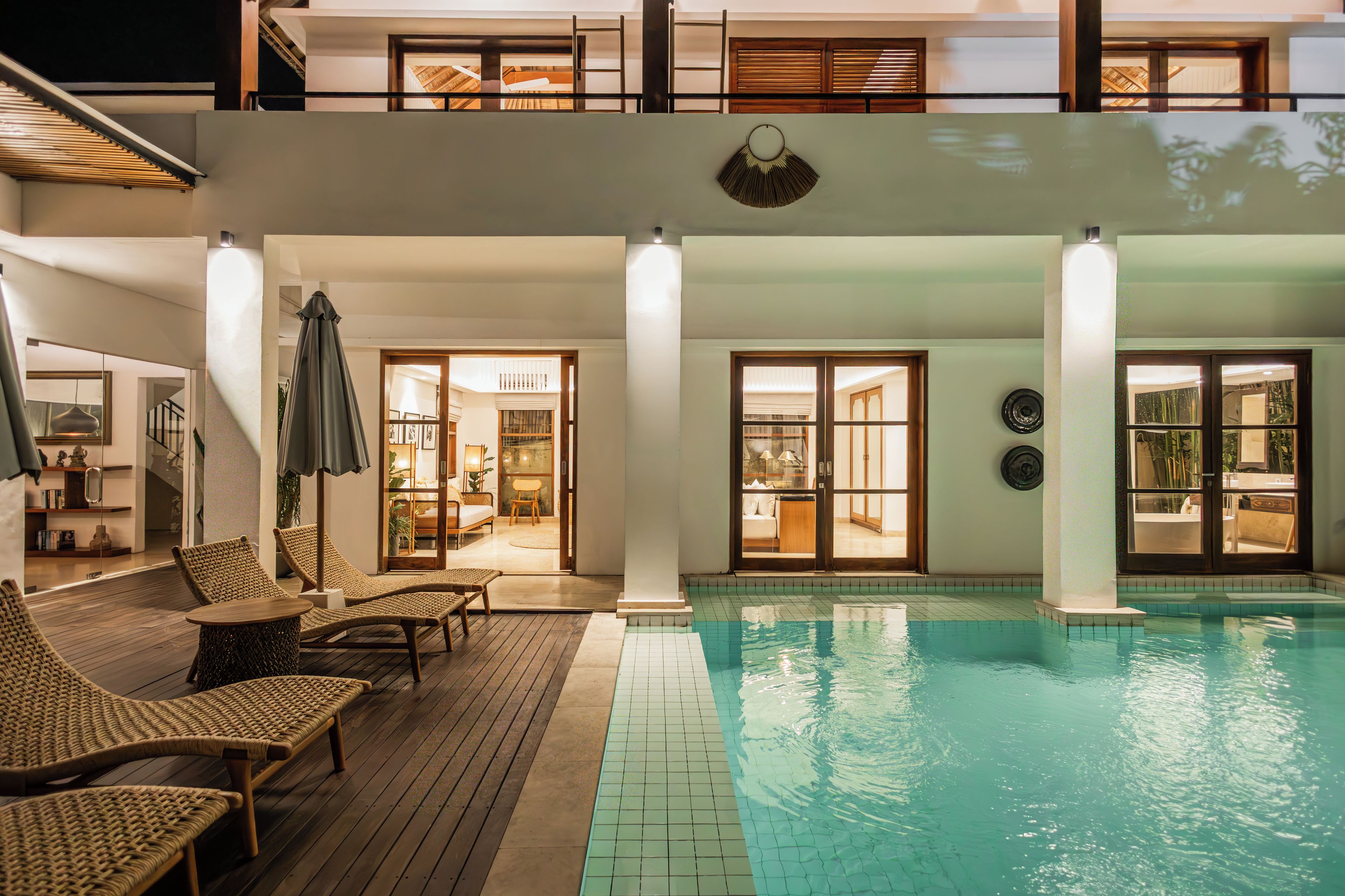 Um edifício de dois andares com piscina, espreguiçadeiras e área de estar coberta.