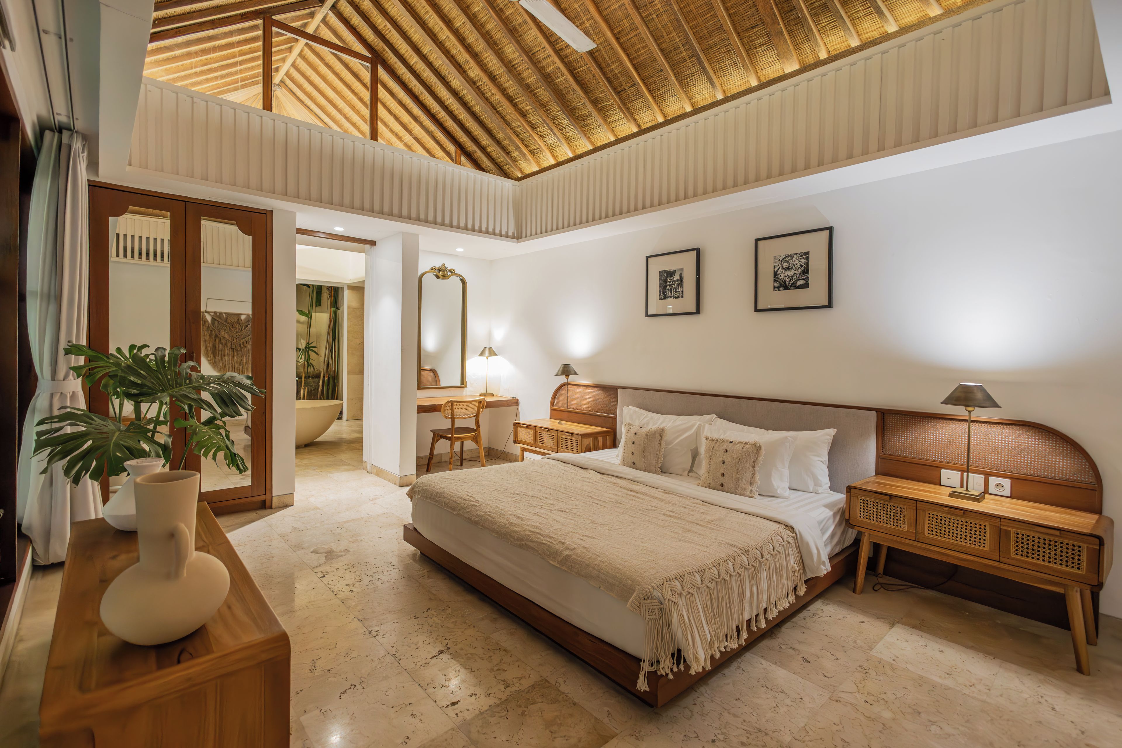 A spacious bedroom with a large bed, bedside tables, a mirror, and a ceiling with a wooden beam design.