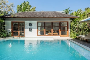 Una casa moderna con piscina, amplios ventanales y plantas tropicales.