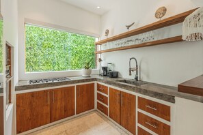 Una cocina con armarios de madera, un ventanal con vistas a zonas verdes y un estante con cristalería.