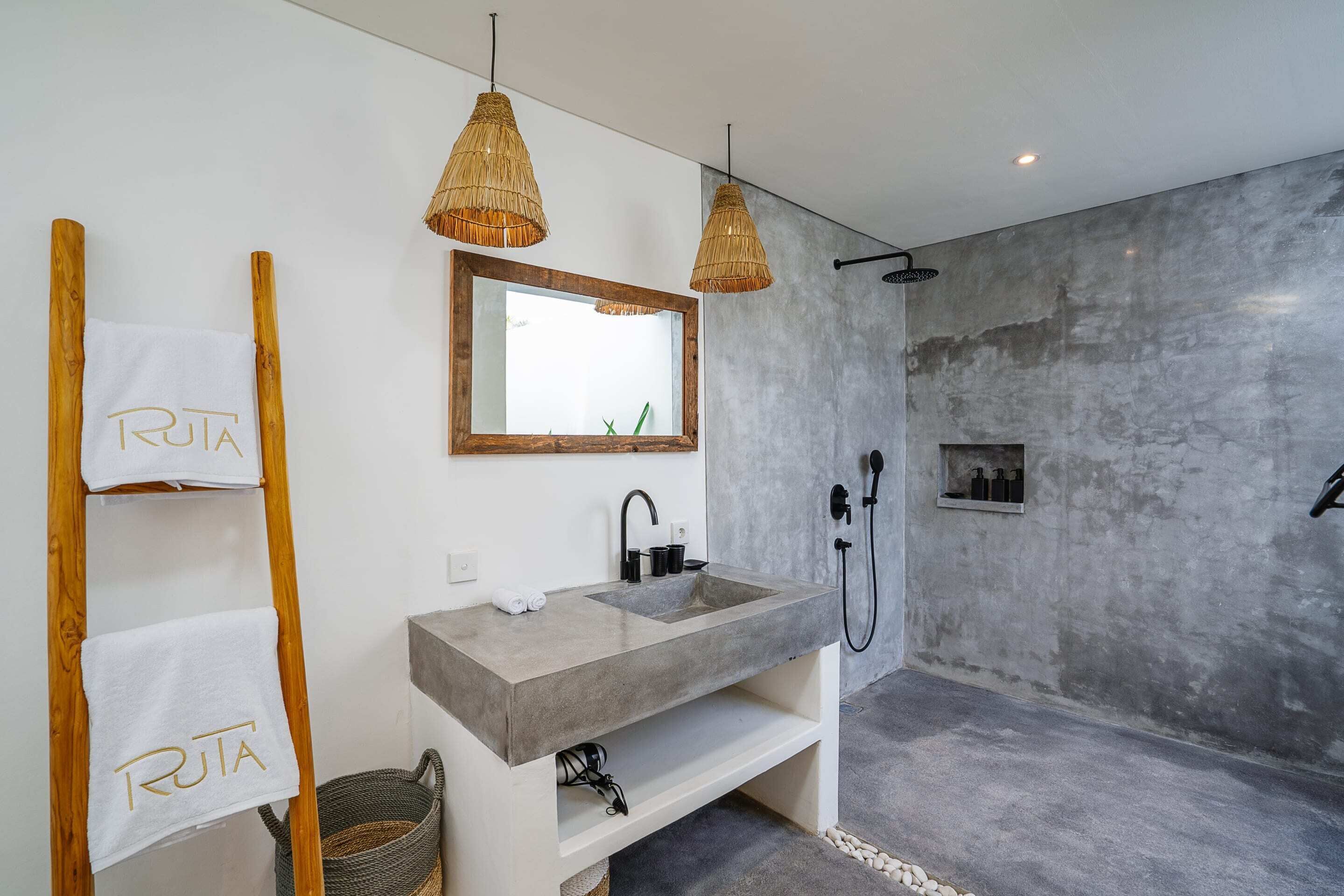 A modern bathroom with a large sink, a mirror, and a shower. There are two towels hanging on a wooden rack and a basket on the floor.