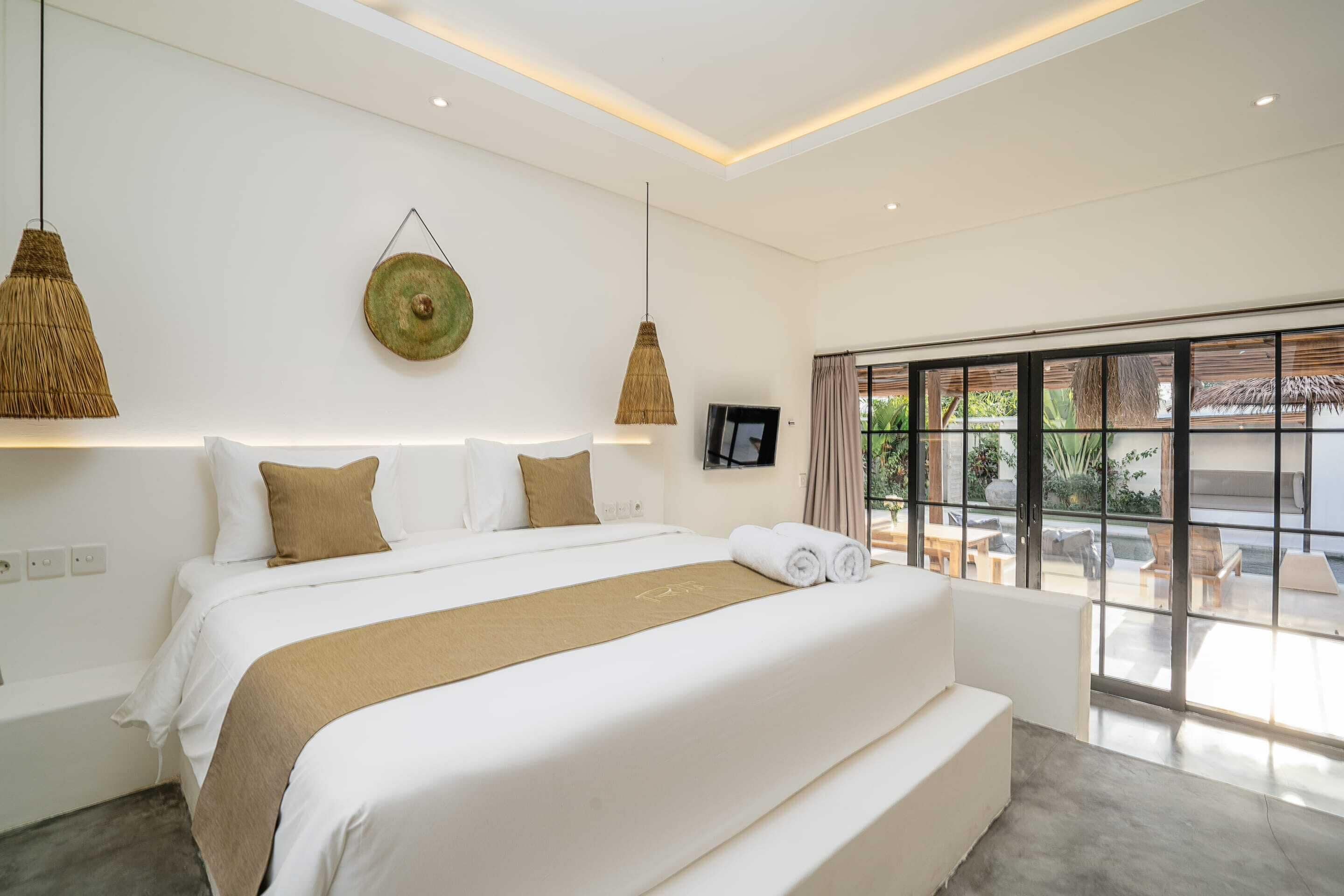 A modern bedroom with a large bed, a TV, and a view of the outdoors through large windows.