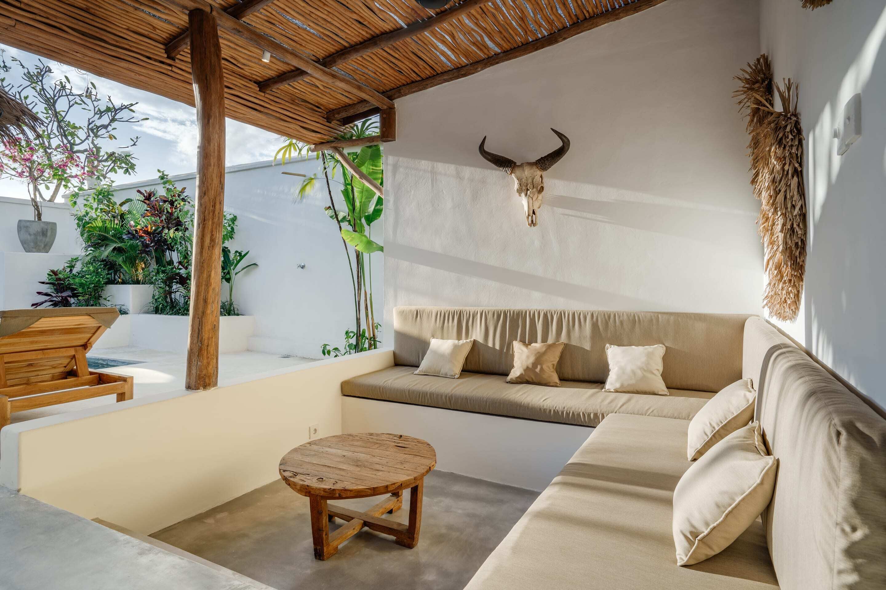 A modern outdoor seating area with a wooden table and a sofa, a bull skull decoration, and potted plants.