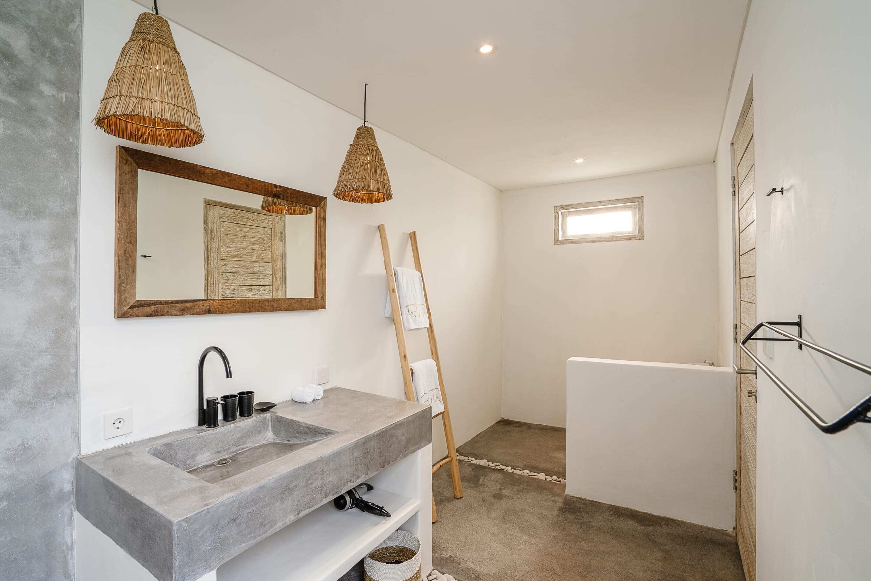 Un baño con lavamanos de hormigón, espejo con marco de madera y una escalera de madera apoyada en la pared.