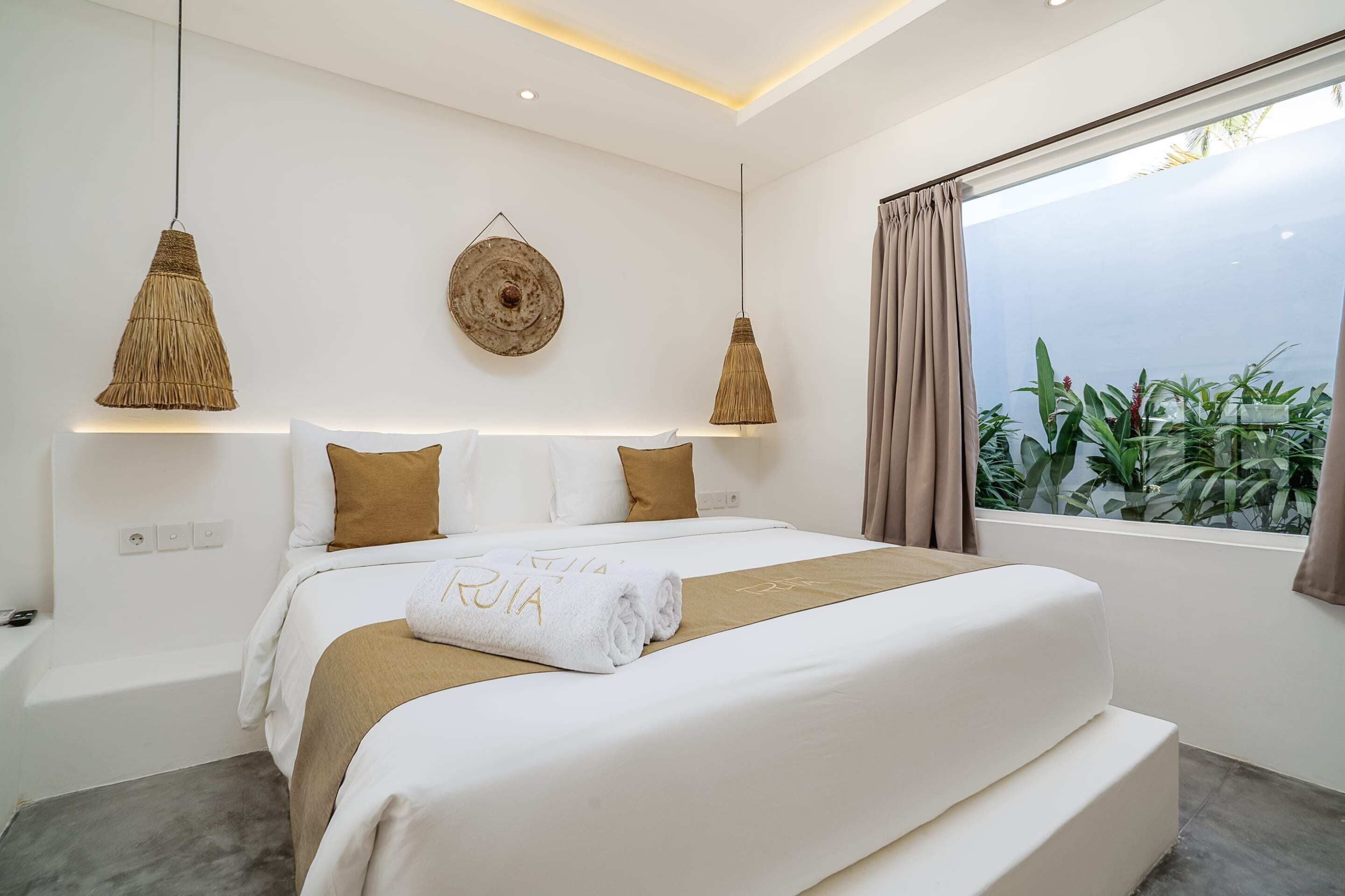 Una camera da letto moderna con un letto grande, due lampade a sospensione, un decoro rotondo al muro e vista sul verde dalla finestra.