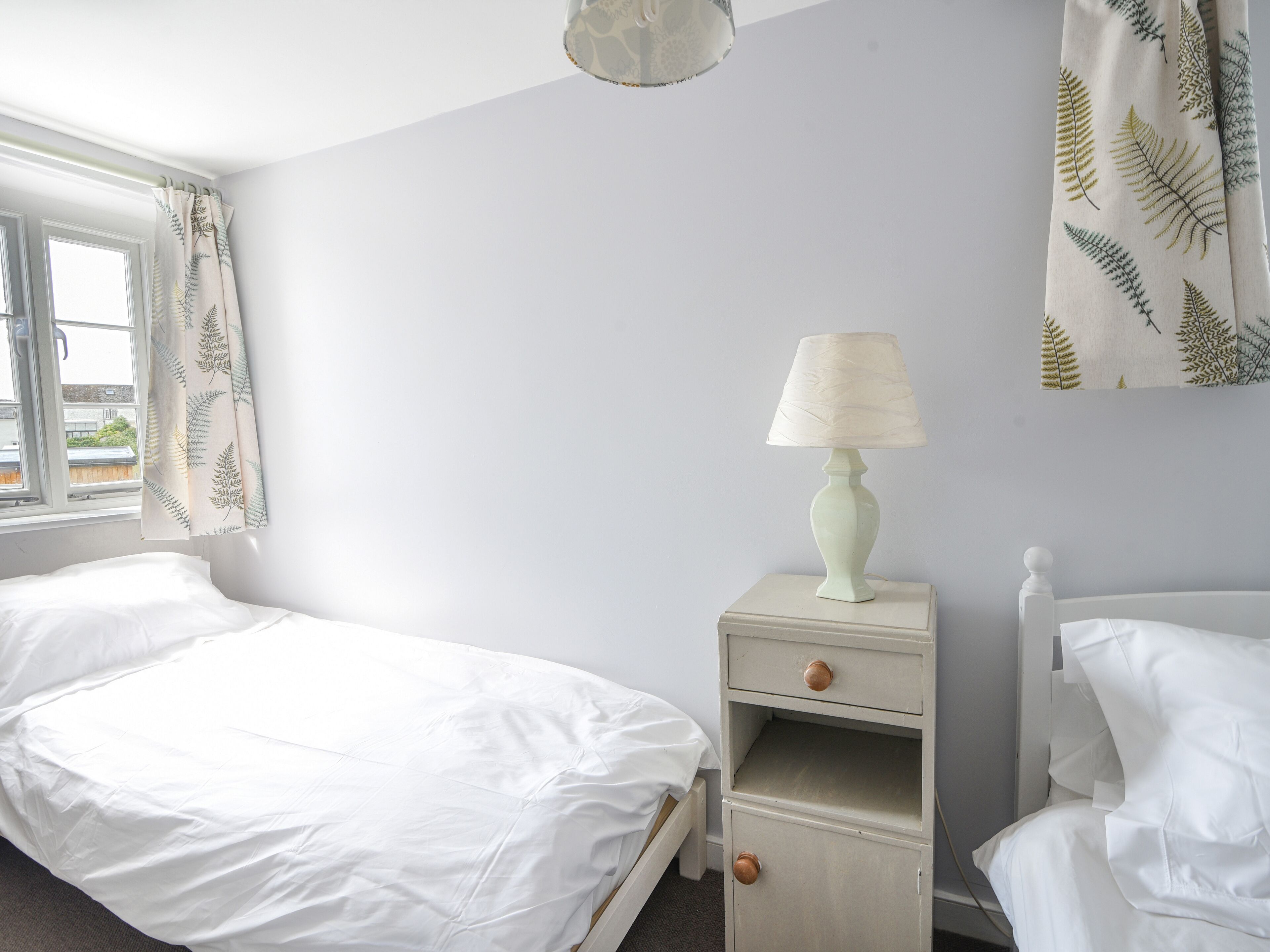 Ein Schlafzimmer mit zwei Betten, einem Nachttisch mit Lampe und einem Fenster mit Vorhängen.