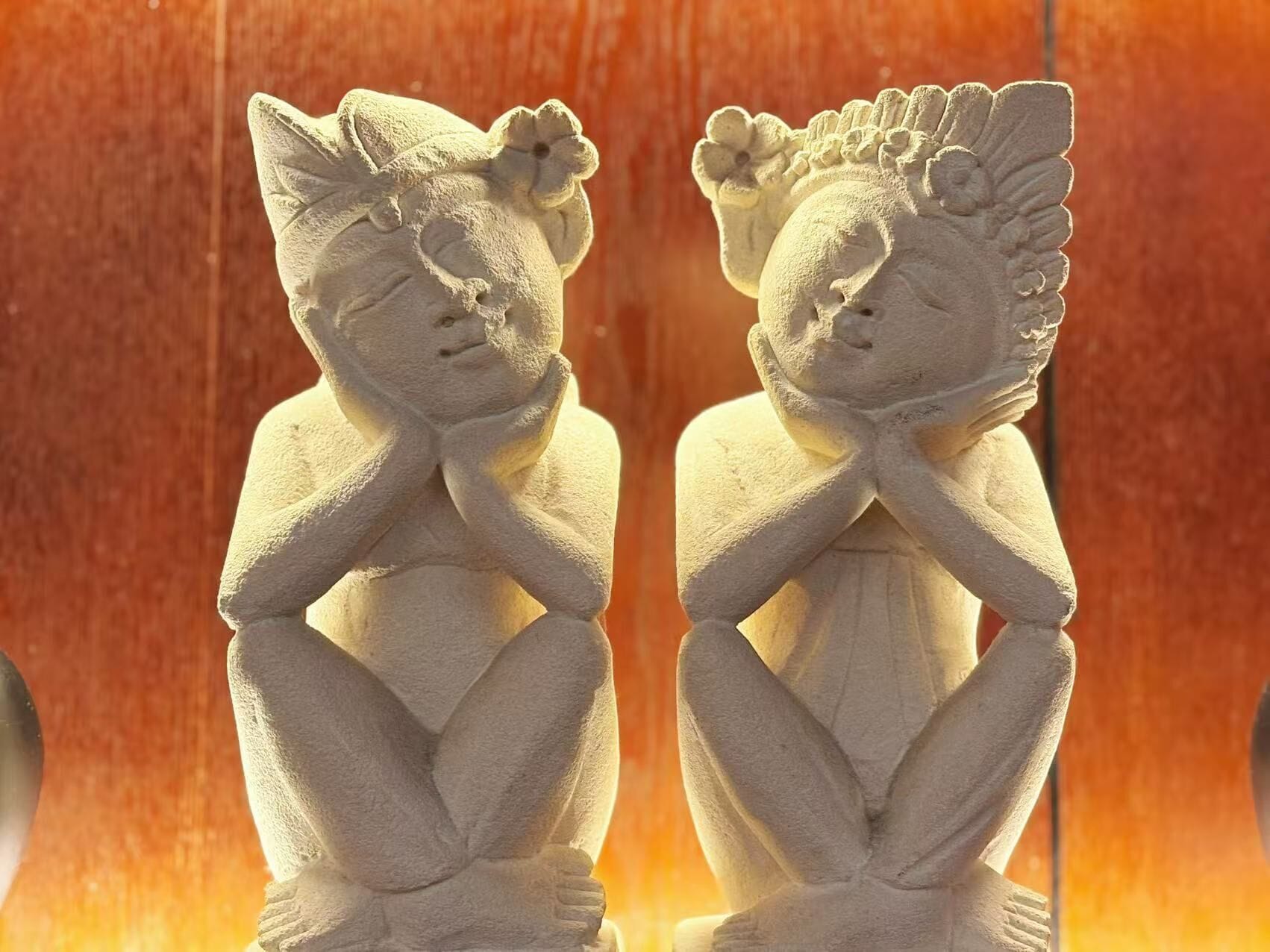 Dos esculturas de piedra idénticas, con adornos florales en la cabeza, situadas frente a un fondo de madera.
