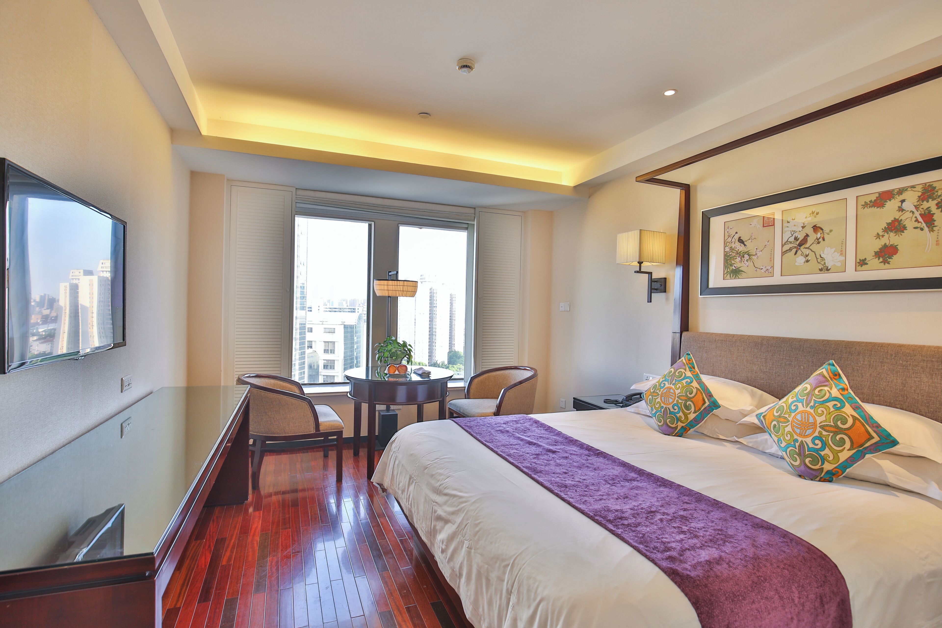 Une chambre d’hôtel avec un grand lit, un bureau avec une chaise, une télévision et une fenêtre avec des stores.