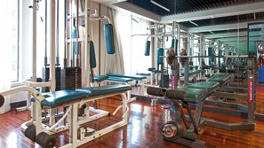 Een sportschool met diverse fitnessapparaten, banken en een houten vloer.