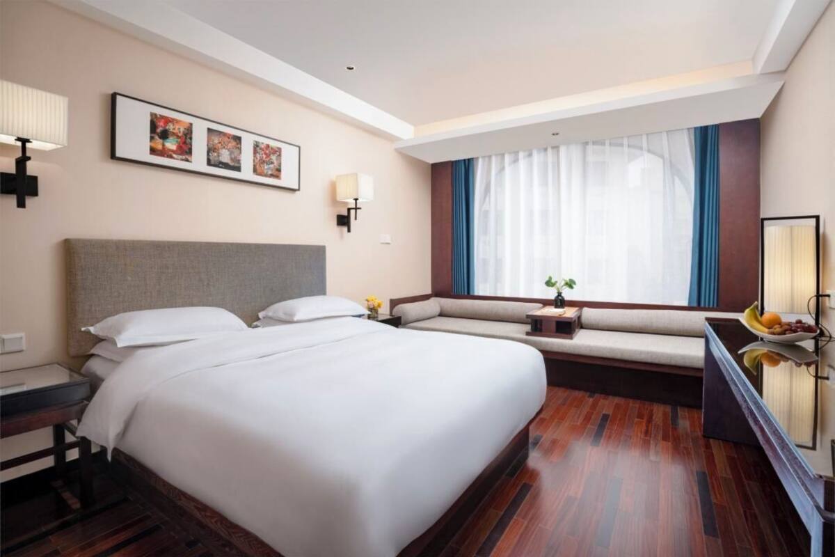 A hotel room with a large bed, a seating area, a desk with a lamp, and artwork on the wall.