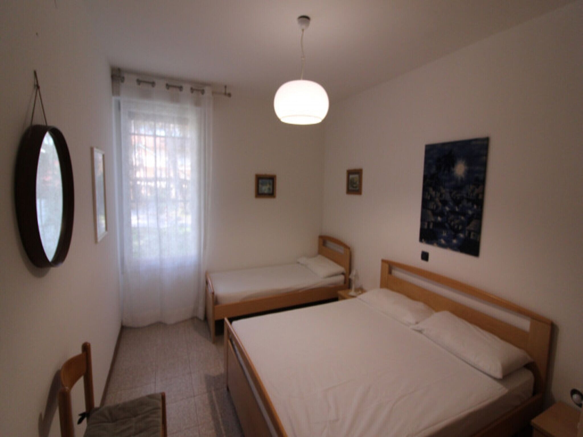 A bedroom with two single beds, a chair, a bedside table, a hanging mirror, and a ceiling light.