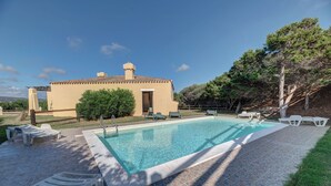 A swimming pool with lounge chairs, a small building, and a tree-lined area. - Charming Sea Villas Es Sleeps 6 With Private Pool Extra bed Possible (Stintino)
