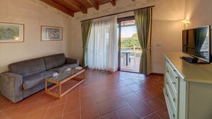 A living room with a sofa, coffee table, TV, and a sliding glass door leading to an outdoor area. - Charming Sea Villas Es Sleeps 6 With Private Pool Extra bed Possible (Stintino)