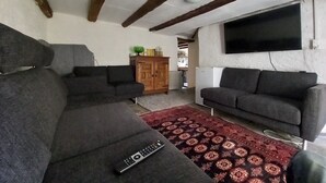 A living room with two sofas, a red patterned rug, a wooden cabinet, and a TV mounted on the wall.