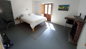 A bedroom with a bed, a desk, a fireplace, and a door leading to another room.