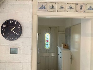 A wall-mounted clock, a door with a stained glass window, and a white wall with decorative tiles.