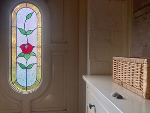 A room with a white door, a round stained glass window with a floral design, and a white cabinet with a woven basket on top.