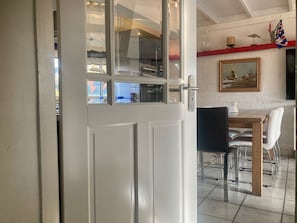 A dining area with a table and chairs, a painting on the wall, and a view through a glass door.