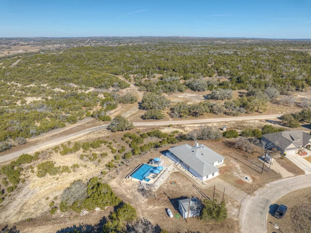 An aerial view of a residential area with a large house featuring a swimming pool, a garage, and a driveway.