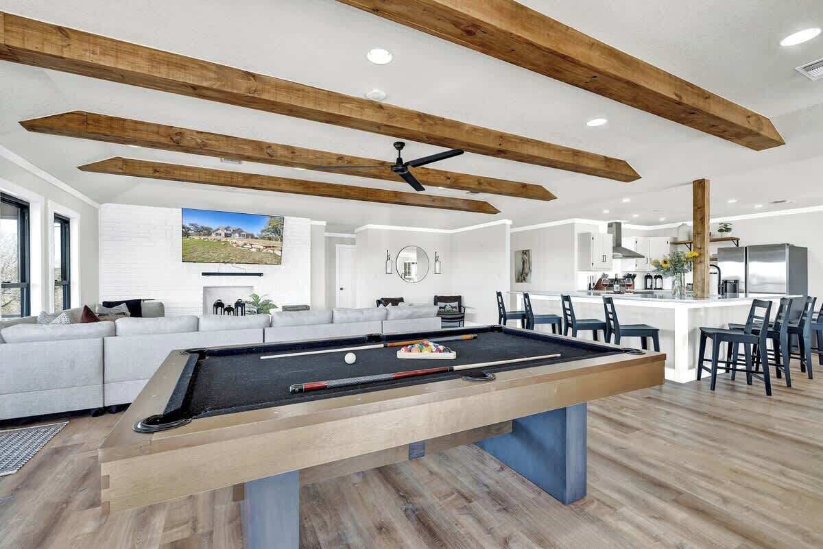 A modern living room with a pool table, a sofa, and a kitchen area in the background.