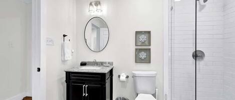 A bathroom with a black vanity, white toilet, and a glass shower enclosure.