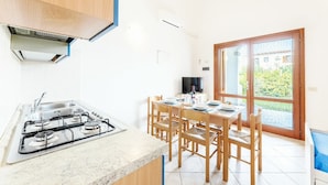 A kitchen with a gas stove, sink, and wooden chairs around a table.