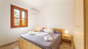 A bedroom with a bed, nightstands, a wardrobe, a window, and an air conditioning unit.
