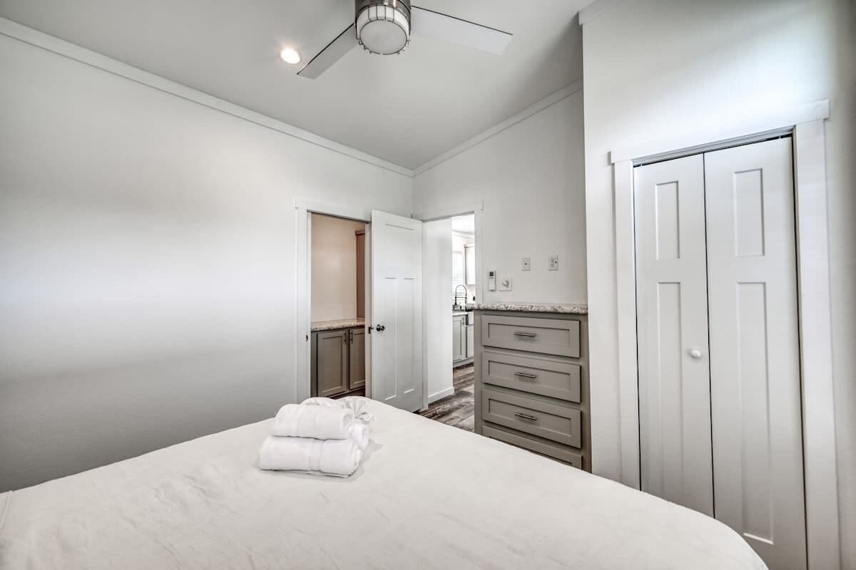 A bedroom with a bed, a dresser, a closet, and a ceiling fan.