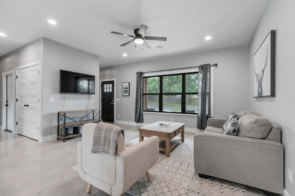 Un salon moderne doté d’un ventilateur de plafond, d’une grande fenêtre avec des rideaux, d’un téléviseur à écran plat et d’un canapé.