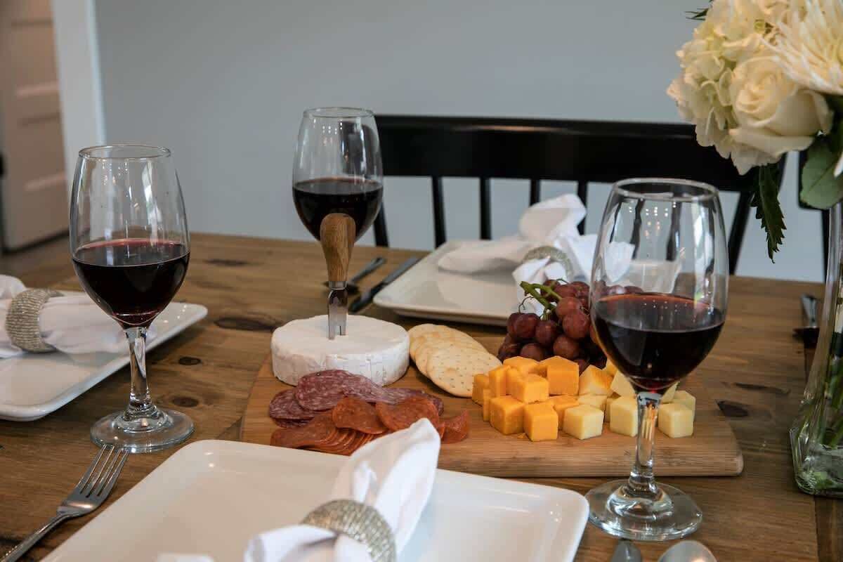 Una mesa dispuesta con copas de vino, queso y embutidos.