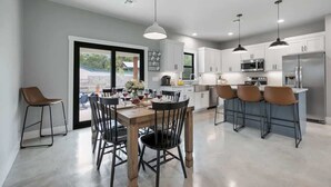 A modern kitchen with white cabinets, stainless steel appliances, and a dining area with a wooden table and chairs. - Luxury Home 3blck From Main St With Firepit (Fredericksburg)