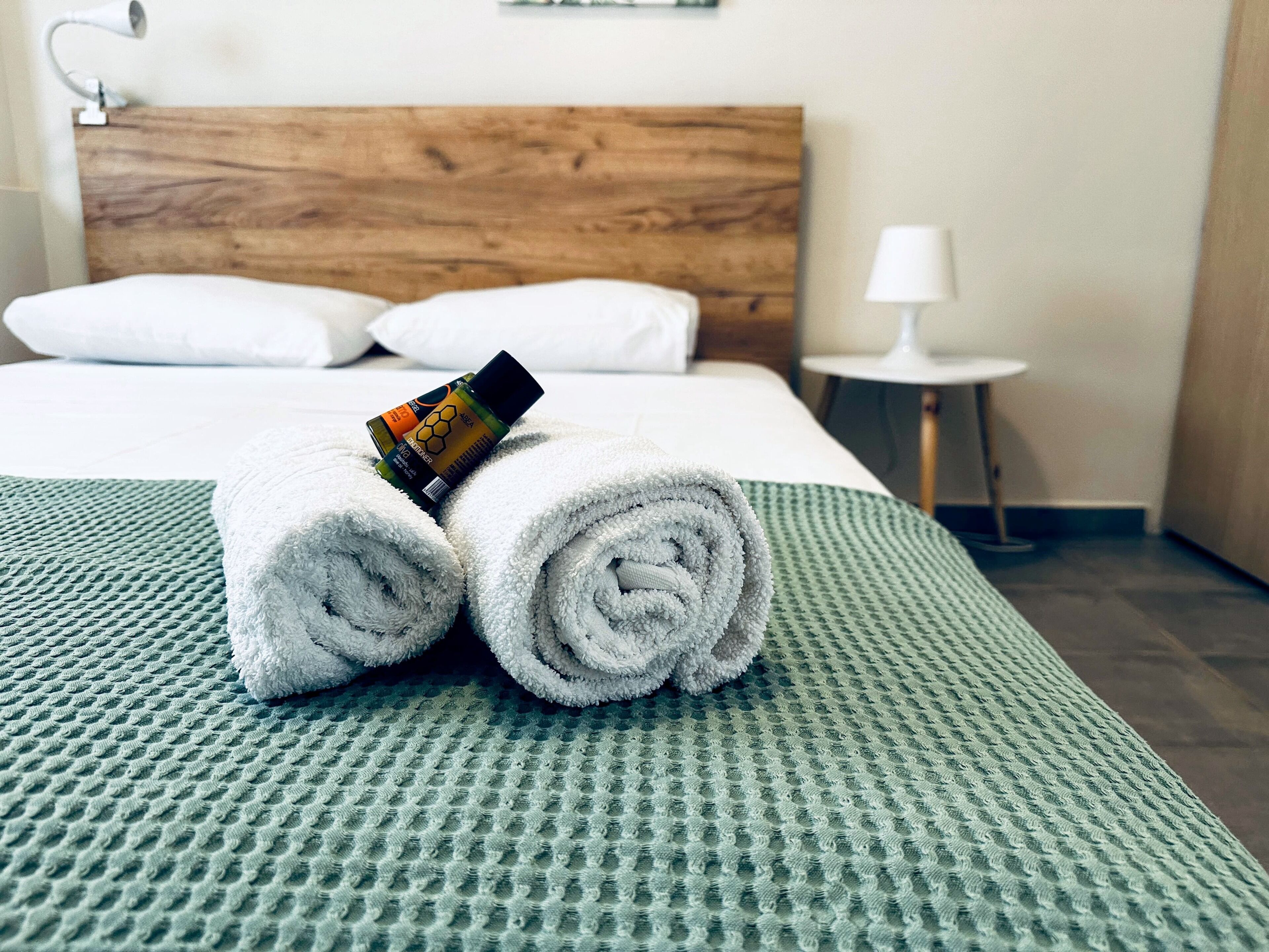 A neatly made bed with rolled white towels and a bottle of lotion on top.