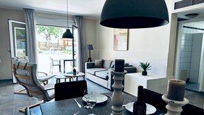Uma área de refeições com mesa posta para dois, um sofá, um abajur e vista para o exterior.
