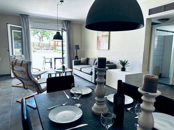 Un coin repas avec une table dressée pour deux personnes, un canapé, une lampe et une vue sur l’extérieur.