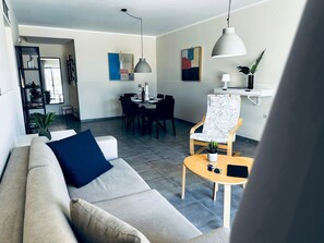 Un salon moderne avec un canapé, une table à manger et des chaises. On y trouve une petite table sur laquelle est posée une plante et une paire de lunettes de soleil.