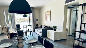 Uma sala de jantar com mesa posta para quatro pessoas, um sofá, uma estante de livros e vista para o exterior.