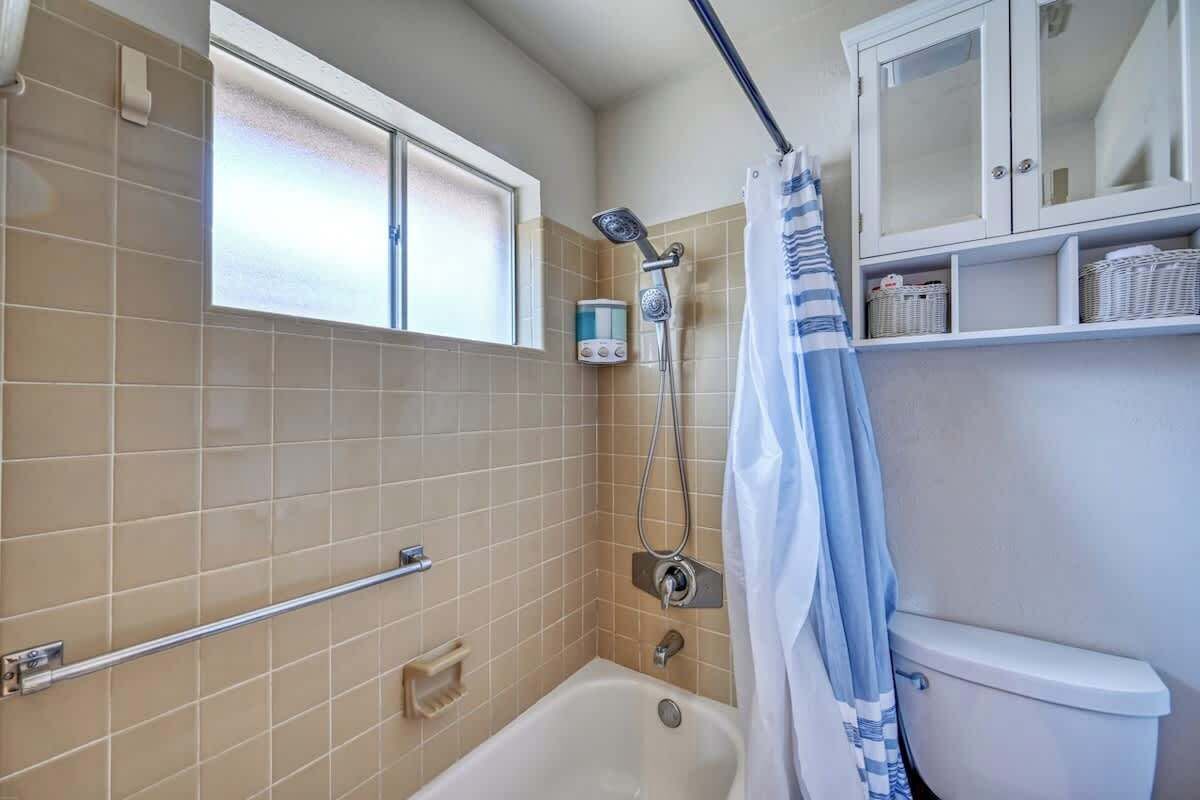 A bathroom with a bathtub, a shower, a toilet, and a window with frosted glass.