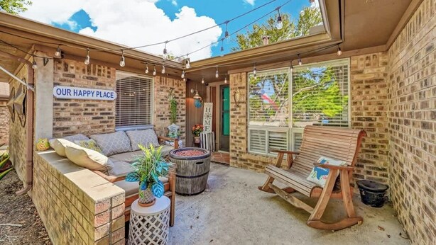 Une agréable terrasse extérieure avec un mur en briques, un banc en bois et un espace salon confortable avec des coussins.