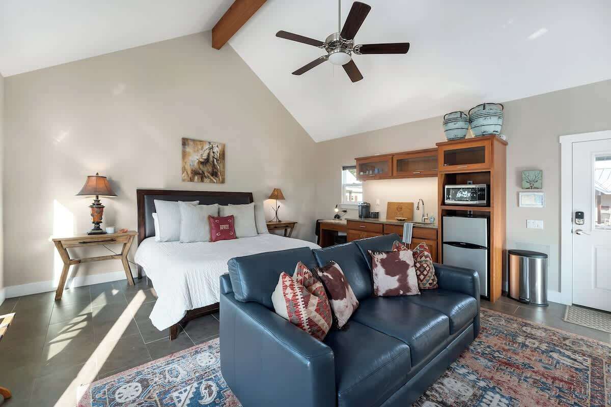 Une chambre avec un lit, un canapé en cuir bleu, un ventilateur de plafond et un coin cuisine équipé de placards et d’appareils électroménagers.