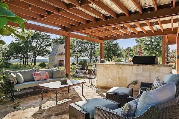 Un patio exterior con chimenea de piedra, mobiliario de mimbre y vistas del paisaje.