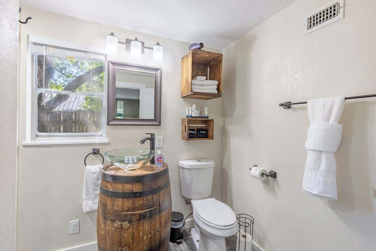 Un baño con un lavabo de barril de madera, un inodoro, una ventana y un perchero para toallas.