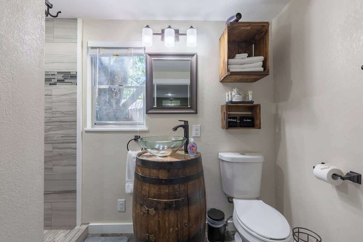 Une salle de bain avec un lavabo en forme de tonneau en bois, des toilettes, une fenêtre et un miroir avec des lumières au-dessus.