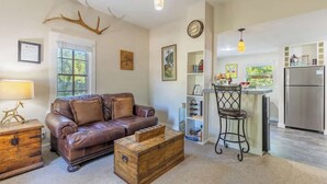 A cozy living room with a brown leather sofa, a wooden chest, and a dining area with a bar.