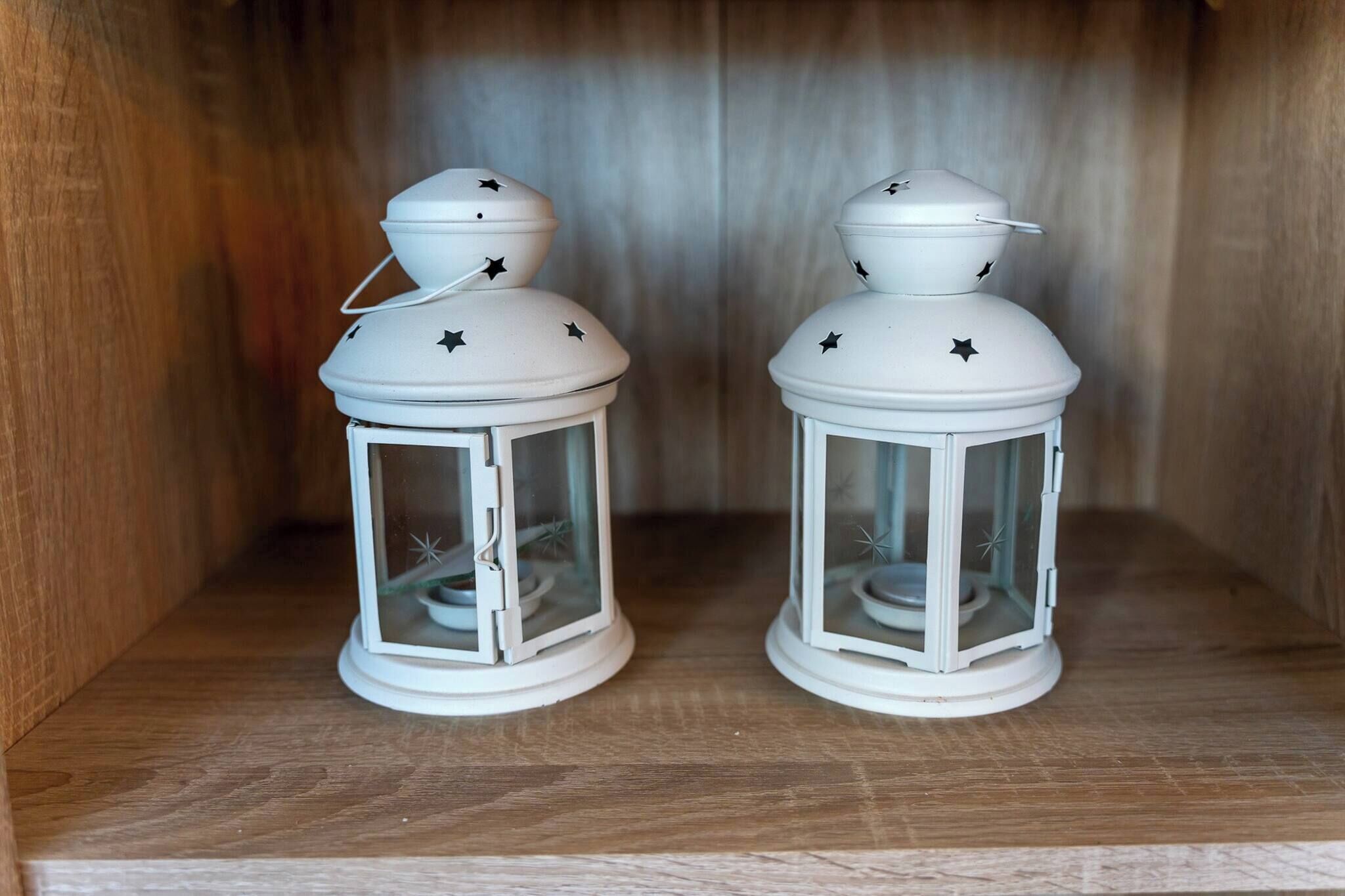 Two white lanterns with star designs on a wooden shelf.