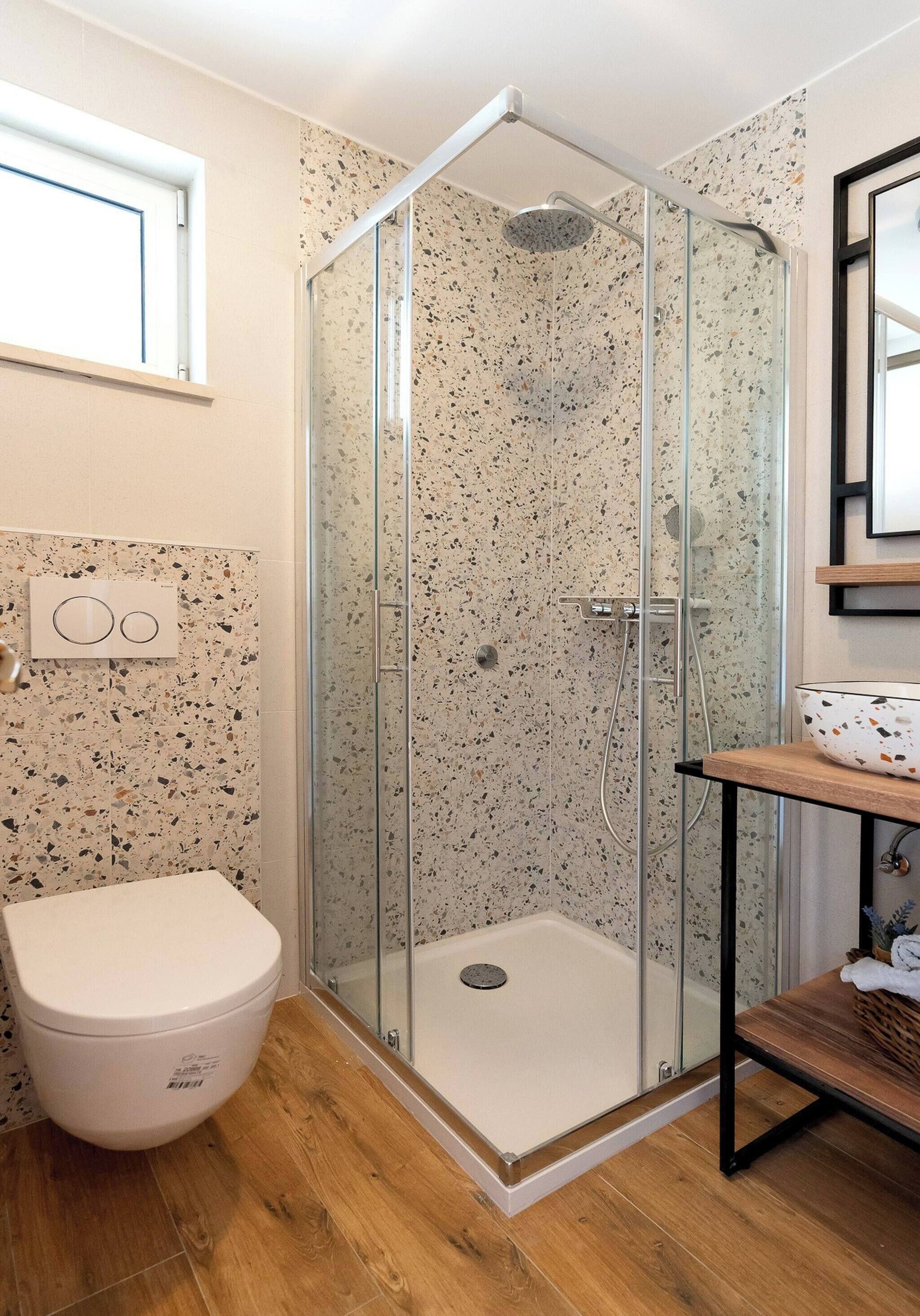 A modern bathroom with a glass-enclosed shower, a white toilet, and a wooden vanity.