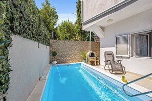 A swimming pool with a brick wall, a stone oven, and two lounge chairs.