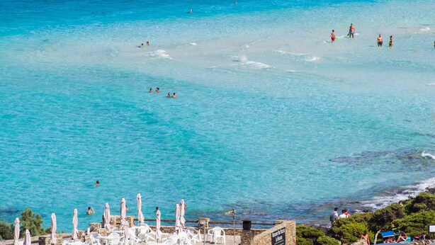 Een strand met helder turquoise water, wit zand en diverse parasols en ligstoelen.