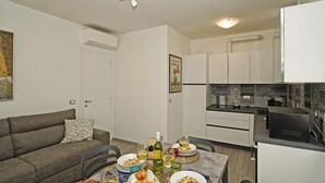A modern kitchen with white cabinets, a dining table set with plates of food and glasses of wine, and a grey sofa in the living area. - Residence Punta Gro 2 5 by Wonderful Italy (Sirmione)