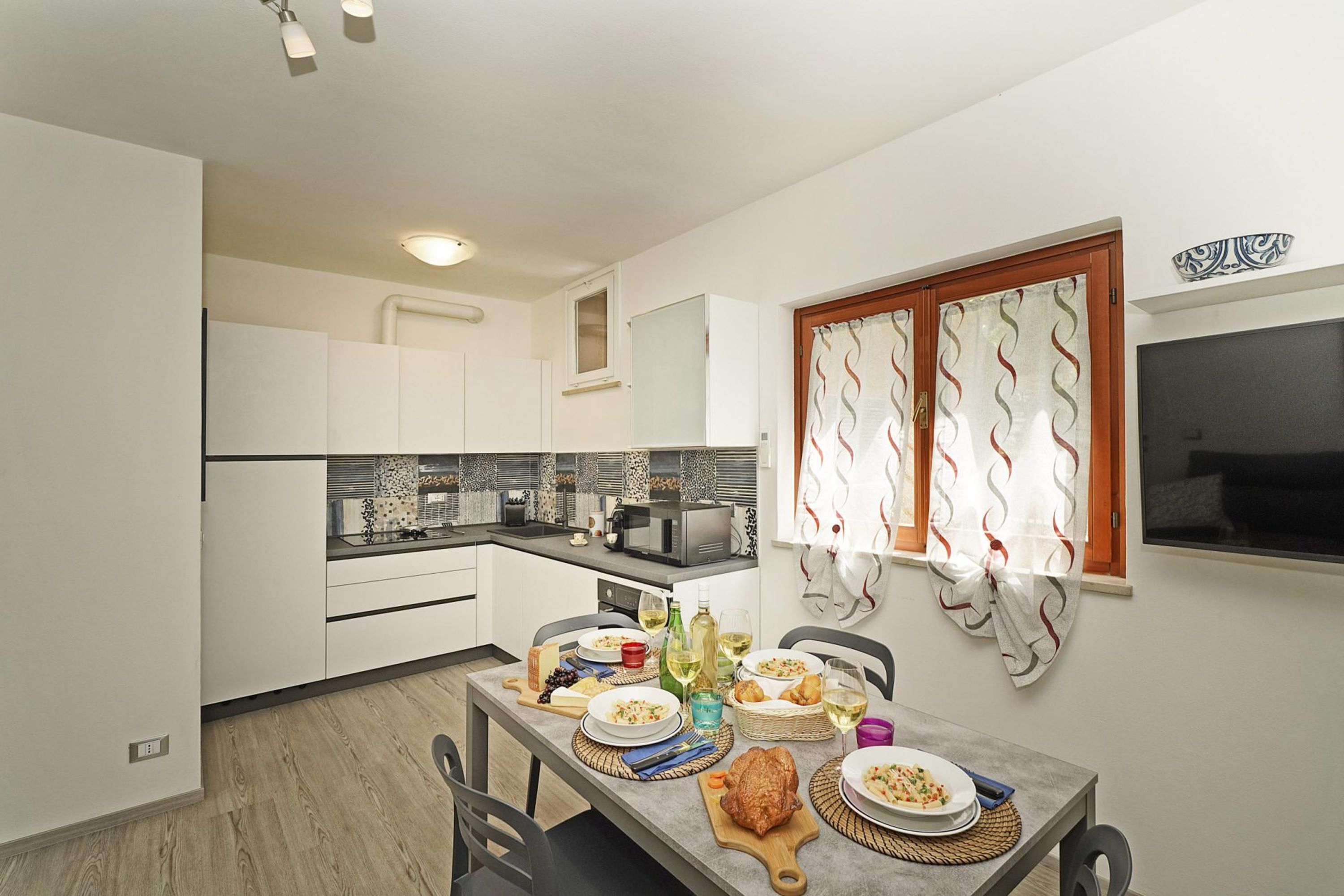 A compact kitchen with white cabinets, a dining table set with plates and glasses, and a window with curtains.